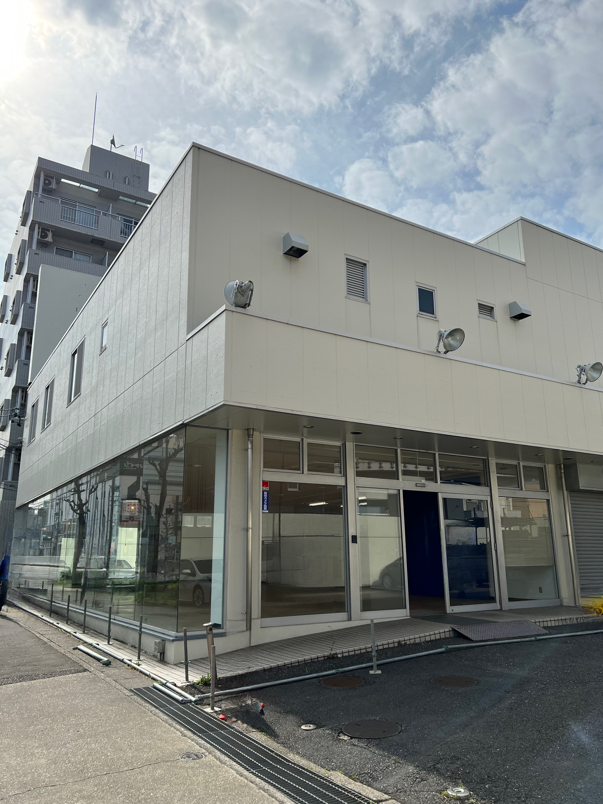 道路沿いに立つ白い平屋店舗のガラス張りファサード